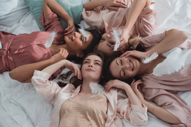 Concentration sélective des femmes multiculturelles reposant ensemble sur le lit avec des plumes à la fête de célibataire
 - Photo, image