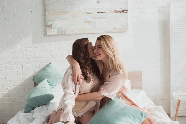 Γυναίκες αγκαλιασμένες και χαμογελαστές με μαξιλάρια στο κρεβάτι στο μπάτσελορ πάρτι - Φωτογραφία, εικόνα