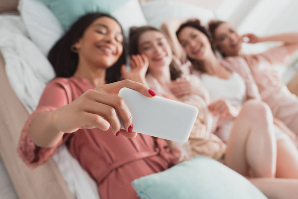 Selectieve focus van Afrikaans Amerikaans meisje nemen selfie met vrienden op bed op vrijgezellenfeest - Foto, afbeelding