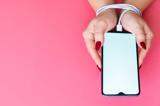 У женщин верхнего вида руки имеют современный смартфон с экраном Blank на розовом фоне. Зависимость от социальных сетей, интернета и гаджетов
 . - Фото, изображение