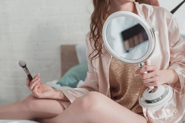 Cropped view of woman with mirror and cosmetic brush in room - Фото, изображение