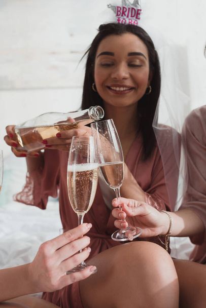 Vista cortada da noiva americana africana derramando champanhe em copos com amigos na festa de despedida de solteira
 - Foto, Imagem