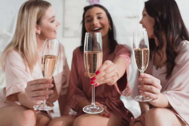 Selective focus of multiethnic women holding champagne glasses and smiling at bachelorette party - 写真・画像