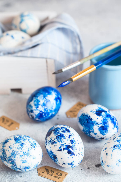 Dyed Easter eggs. Classic blue 2020 Easter eggs on the grey background. Blue speckled easter eggs with paint and brushes. Decorating eggs, preparing for Easter - 写真・画像
