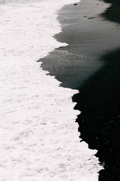 a sea wave arrives on the shore with black volcanic sand . - Photo, Image