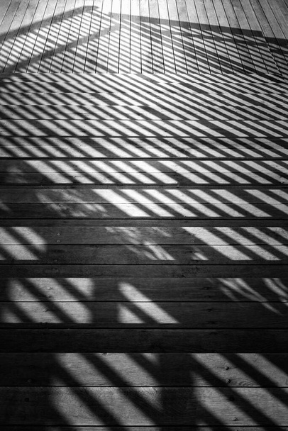 Staircase with a shadow from the railing. Close-up fragment of a staircase leading downstairs with wooden steps and metal railing. A play of light and shadow in the evening. Conceptual image. - Photo, Image