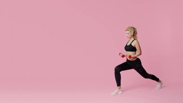 Fitness girl with perfect slim and fit body training muscles with dumbbells on pink background. Sporty woman in sportswear - Photo, Image