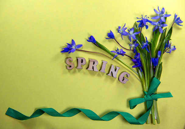 Bouquet frische Blumen von Blauglocken mit grünem Band auf gelbem Hintergrund. Wortfeder aus Holzbuchstaben. Draufsicht, flache Lage, Kopierraum. - Foto, Bild