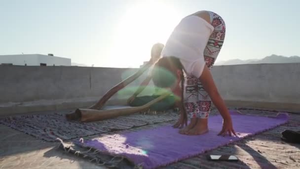 Chica práctica de pie hacia adelante doblar postura de yoga mientras el hombre juega didgeridoo
 - Metraje, vídeo