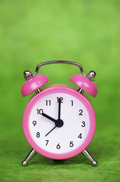 Zeit sparen, Sommerzeit-Konzept, pinkfarbener Wecker auf grünem Hintergrund. Kopierraum. - Foto, Bild