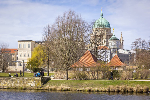 Kilátás a történelmi épület belvárosában Potsdam, Brandenburg. Az előtérben a Havel folyó látható a Barátság-sziget mögött, egy gyönyörű zöld park mögött. A háttérben egyértelműen a Szent Miklós templom kupolája. A babakocsik tavasszal járnak. - Fotó, kép