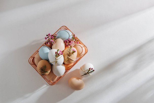 Natural Colored Eggs and flowers in basket with sunlights. Stylish Compositions in pastel colors.  Easter concept. - 写真・画像