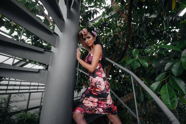 A young beautiful brunette poses near a spiral staircase in the Botanical garden among the dense thickets of the tropic forest. Spa - Foto, imagen