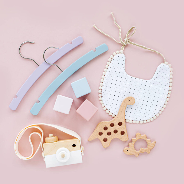 Colorful baby hangers, bib with wooden toys and teether. Set of baby stuff and accessories for newborn on pastel pink background.  Baby shower concept.  Flat lay, top view - 写真・画像