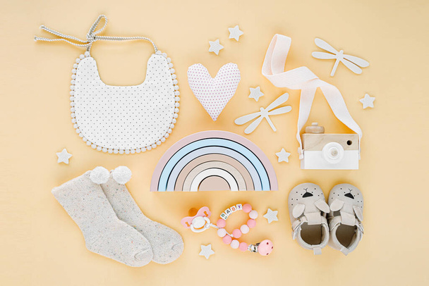 Toys, bib, socks, slippers and rainbow for newborn on yellow background.  Set of  gender neutral baby stuff and accessories. Flat lay, top view  - Φωτογραφία, εικόνα