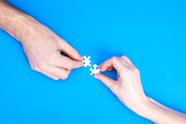 Hands of man and woman collect puzzles on a blue background background. Conceptual image of joint cooperation in the family. View from above - 写真・画像