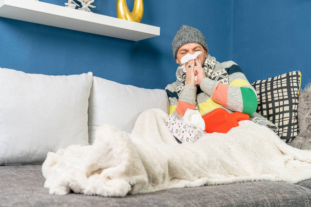 Un hombre con gripe en un sofá se está sonando la nariz en un pañuelo.
 - Foto, Imagen