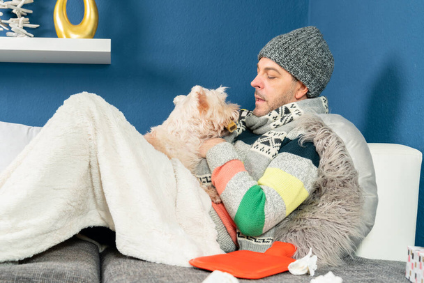 a man with flu cuddles with his dog on the couch - Фото, изображение