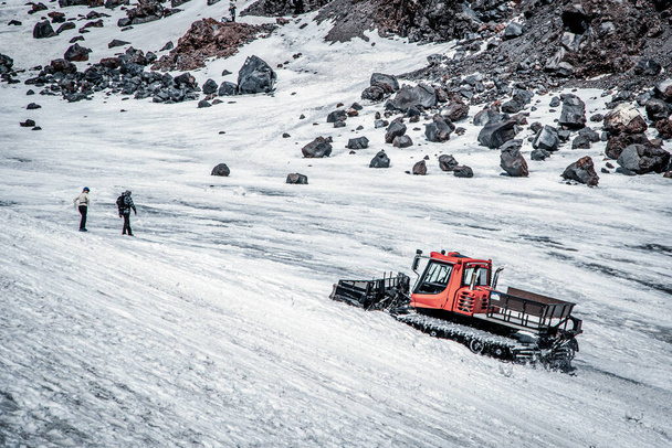 氷河上の赤い雪猫(雪のグルーマー)の閉鎖。エルブラス山、コーカサス、ロシア前に2つのアルピニストの交差点。背景に岩. - 写真・画像