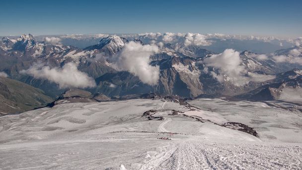 Widok na ośnieżone wzgórze Elbrus, Kaukaz, Rosja. Ścieżka prowadząca od góry. Chmury i góry w tle. - Zdjęcie, obraz