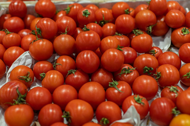 葉が付いている小さな赤いチェリートマト、トップビュー。スーパーの箱の中の熟した赤いトマトの山。食料品店の新鮮な野菜部門 - 写真・画像