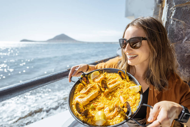 Mujer comiendo comida de mar cerca del océano
 - Foto, Imagen
