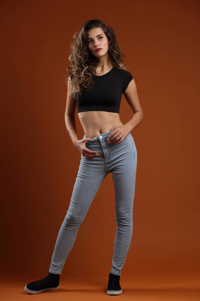 Studio growth portrait of a beautiful slender girl in a black top and blue jeans - Fotografie, Obrázek