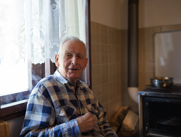 Portrait of smiling senior man sitting beside window in vintage kitchen - Photo, image