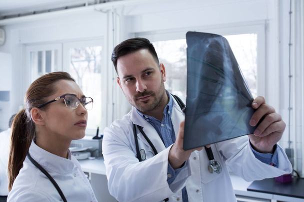 Два врача мужского и женского пола смотрят на рентген в лаборатории - Фото, изображение