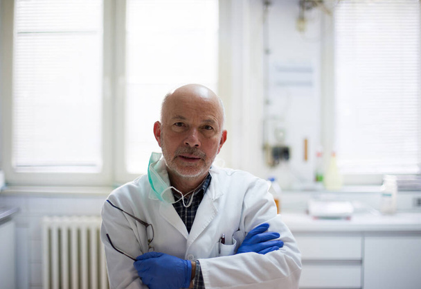 A laboratóriumban keresztbe tett karokkal álló, védőmunkaruhás vezető biológus portréja - Fotó, kép
