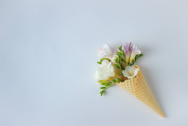 boeket van delicate bloemen in een wafelbeker voor ijs op een witte achtergrond, bovenaanzicht, groot, zomer en lente minimalisme - Foto, afbeelding