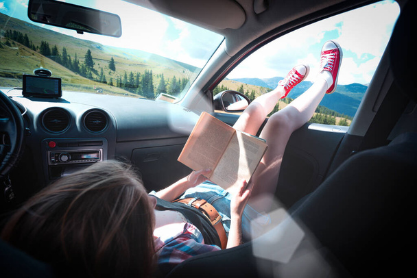 Summer Road Trip. Happy beautiful girl traveling in a car.  reads a book across  at the mountain - Fotografie, Obrázek
