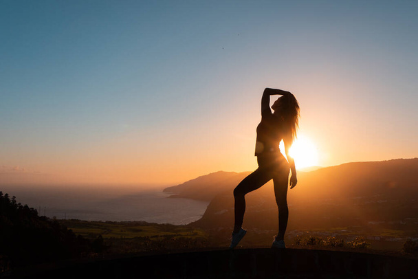 Силует жінки, насолоджуючись свободою, відчуває себе щасливим на заході сонця з горами та морем на фоні
 - Фото, зображення