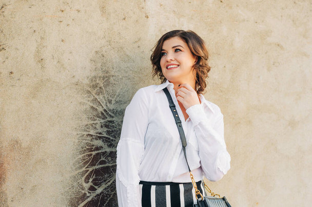 Outdoor fashion portrait of beautiful woman wearing white blouse and black leather cross body bag - Foto, Imagen