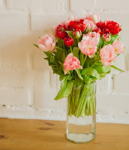 Glass vase with bouquet of beautiful tulips on brick wall background - Photo, image