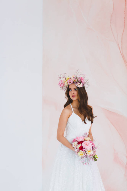 Young bride in white dress with flower wreath on her head posing in the studio - Foto, Imagen