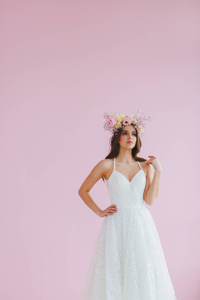 Young bride in white dress with flower wreath on her head posing in the studio - Foto, Imagem