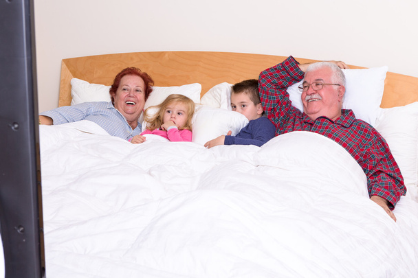 Abuelos viendo la televisión en la cama con sus nietos
 - Foto, imagen