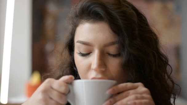 beautiful brown-haired girl drinks a delicious and bitter cappuccino in a restaurant - Video