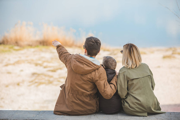 joven hermosa familia sentada en la playa con vista al lago. temporada de otoño - Foto, Imagen