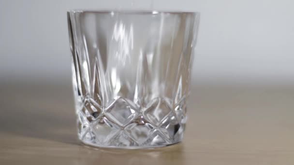 IJsblokjes vallen in een glas. IJs in een glas. Leeg kristalglas. - Video