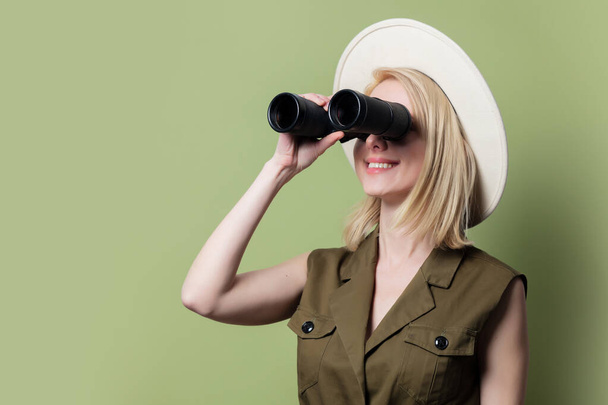 Styl blondýny žena s dalekohledem, klobouk a sluneční šaty na zeleném pozadí - Fotografie, Obrázek