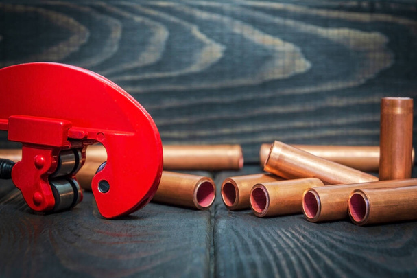 Cortador de tubos vermelho e tubos de cobre com conectores para reparos de encanamento em placas de madeira vintage preto de perto
 - Foto, Imagem