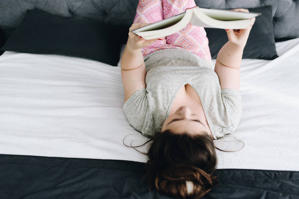 Молода біла сексуальна жінка на спині читає книгу на своєму ліжку
 - Фото, зображення