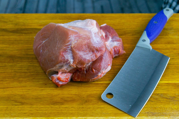 Um machado para carne fica ao lado de um grande pedaço suculento de porco
. - Foto, Imagem