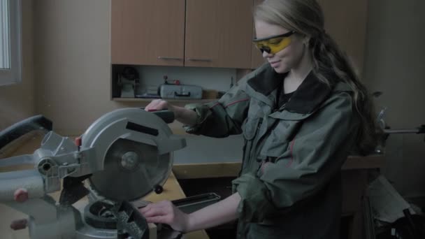 Mädchen in einer Werkstatt sägt Holzmaterialien und lächelt - Filmmaterial, Video