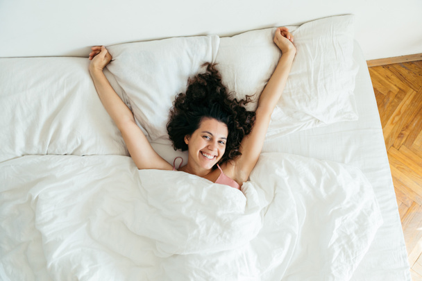 jovem mulher bonita na cama com folhas brancas espaço cópia de luz brilhante
 - Foto, Imagem