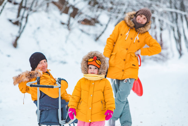 familia joven jugando juntos al aire libre en el día de invierno nevado abrigos amarillos familia se ve - Foto, Imagen