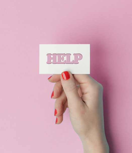 Help word written on a piece paper in hand on pink background - Zdjęcie, obraz