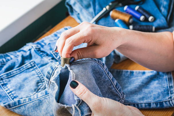 A woman is repairing ripped blue jeans. The concept of economical reuse of things. Homemade needlework. - Photo, Image